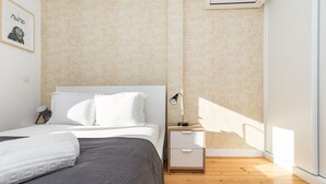 A modern bedroom with a bed, bedside table, and a window with sunlight. - Belem Design 08 by Homing (Lisbon)