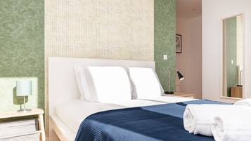Uma cama bem arrumada com lençóis brancos e um espalha azul, uma luminária de cabeceira e um espelho na parede.