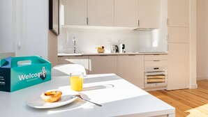 A modern kitchen with white cabinets, a countertop, and a toaster. There is a glass of orange juice and a muffin on a white plate. A blue 'Welcome' box is visible on the left. - Belem Design 09 by Homing (Lisbon)