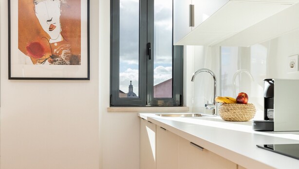 A modern kitchen with a white countertop, a stainless steel sink, and a basket of fruit. - Belem Design 09 by Homing (Lisbon)