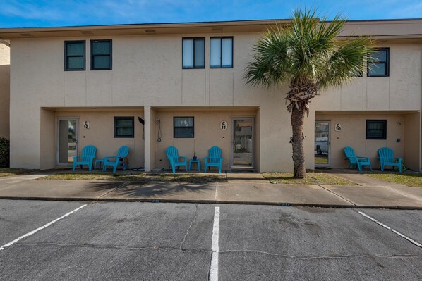 A building with numbered doors, outdoor seating, and a palm tree. - Sugar Beach C-11 (Navarre)