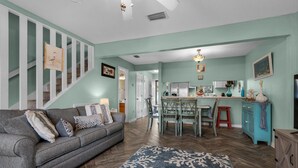 A living room with a sofa, a patterned rug, a staircase, and a kitchen area with a dining table and chairs. - Sugar Beach C-11 (Navarre)