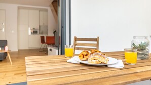 Una mesa de desayuno con pasteles y jugo de naranja, una silla de madera y una cocina al fondo.