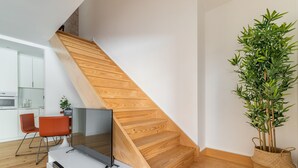 Una cocina moderna con armarios blancos, una escalera de madera, un televisor de pantalla plana sobre un mueble blanco y una planta en maceta.