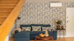 A living room with a blue sofa, a wooden coffee table with fruit, and patterned wallpaper. - Belem Design 12 by Homing (Lisbon)
