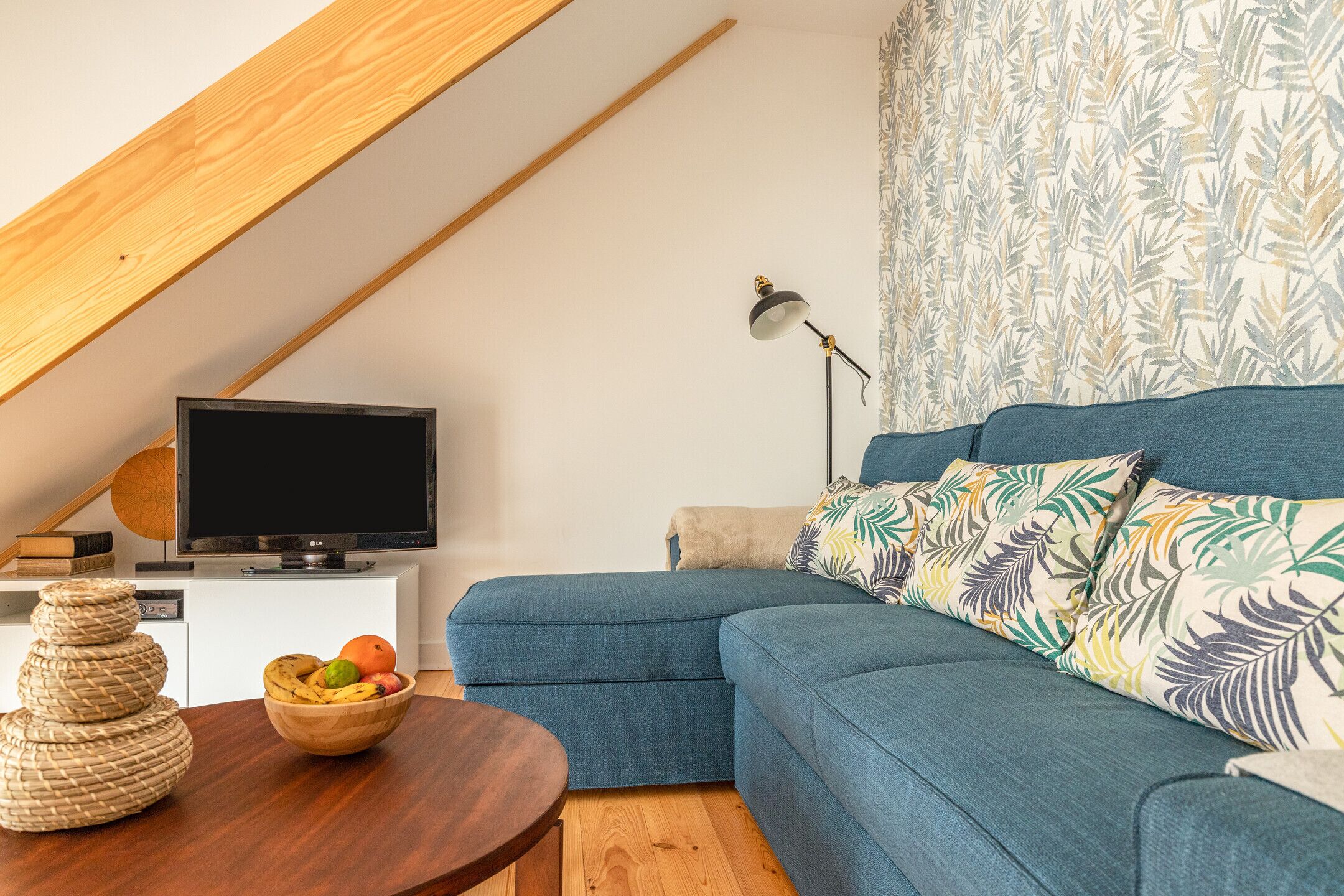 A modern living room with a sectional sofa, a wooden coffee table, a TV on a white stand, and a patterned curtain.