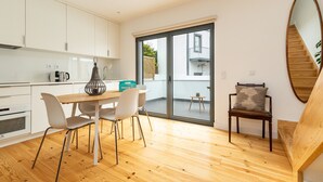 A modern kitchen with white cabinets, a wooden dining table, and a sliding glass door leading to a balcony. - Belem Design 12 by Homing (Lisbon)
