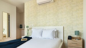 A neatly made bed with white linens, a bedside table with a lamp, and a wall-mounted air conditioner. - Belem Design 12 by Homing (Lisbon)