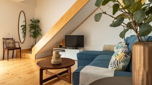 A modern living room with a sloped ceiling, a blue sofa, a wooden coffee table, a television, and a plant. - Belem Design 12 by Homing (Lisbon)