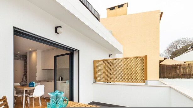 A modern outdoor patio with a dining table and chairs, a glass door leading to a kitchen, and a decorative screen. - Belem Design 12 by Homing (Lisbon)