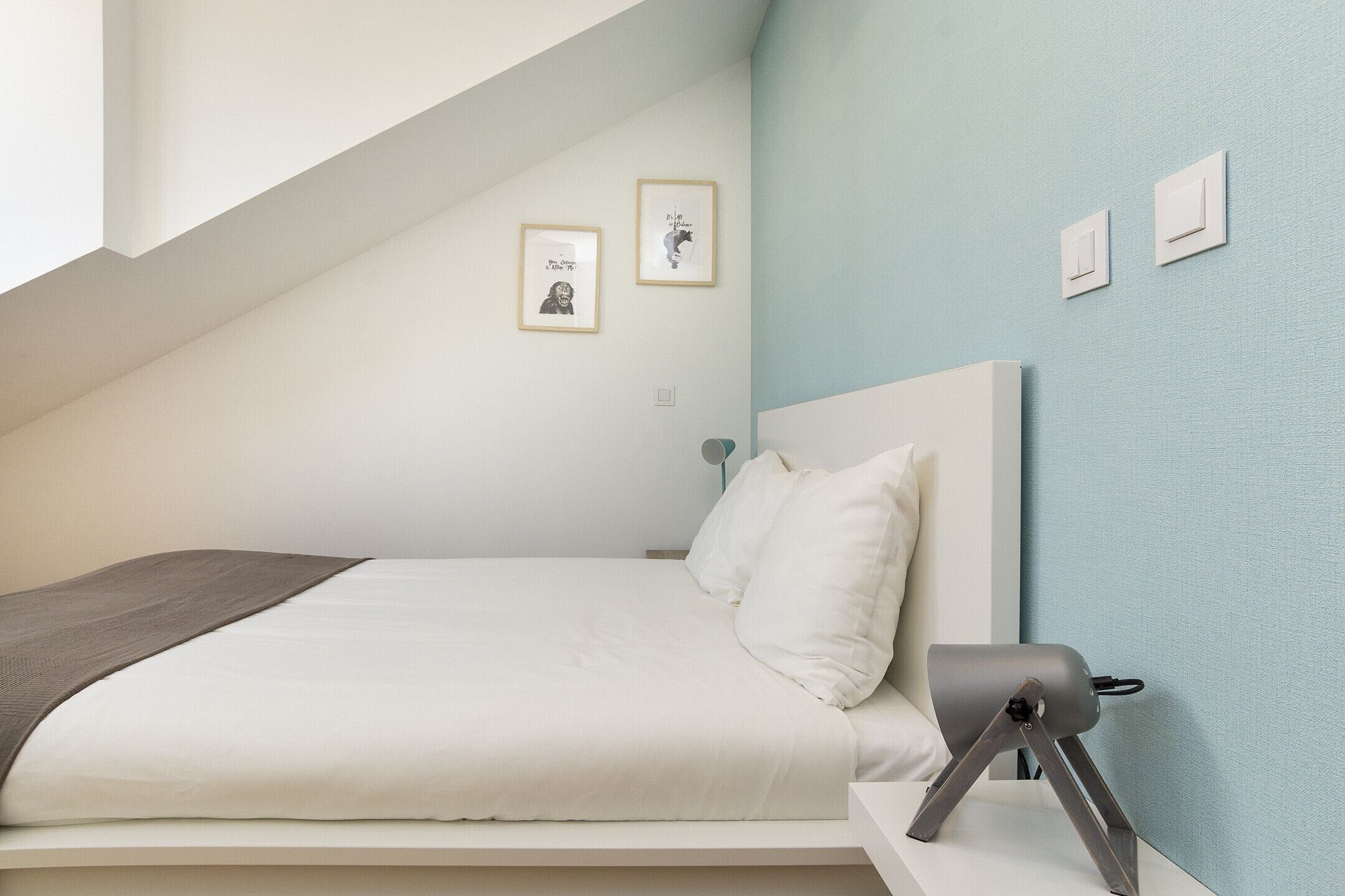 A bedroom with a bed, a bedside lamp, and two framed pictures on the wall.