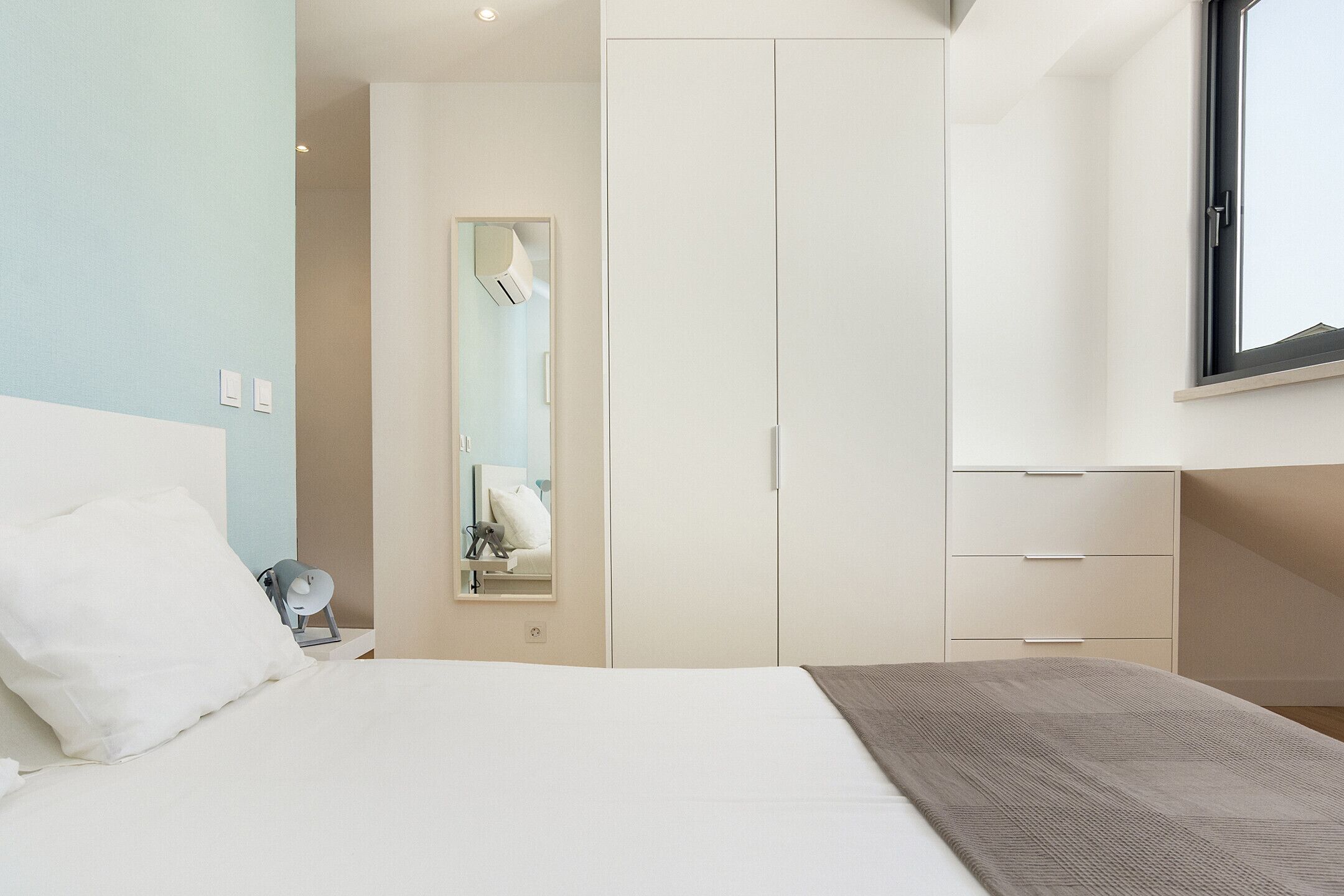 A modern hotel room with a large bed, a wardrobe, a mirror, and a window.