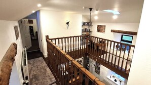 Un interior con varios niveles, una escalera de madera, una zona de cocina con estufa y fregadero, y una estantería.
