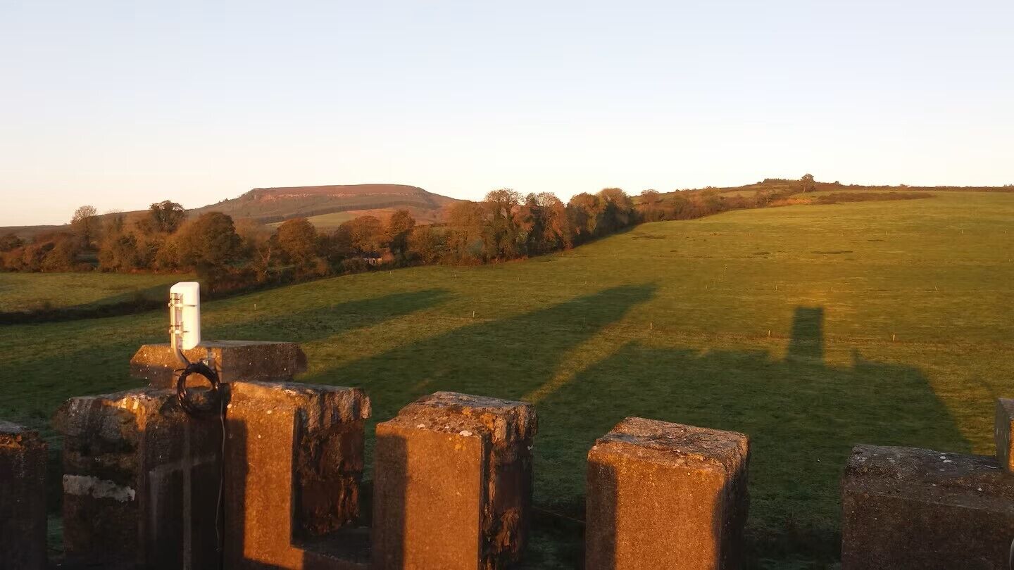 A rural landscape with a grassy field and a stone fence in the foreground.