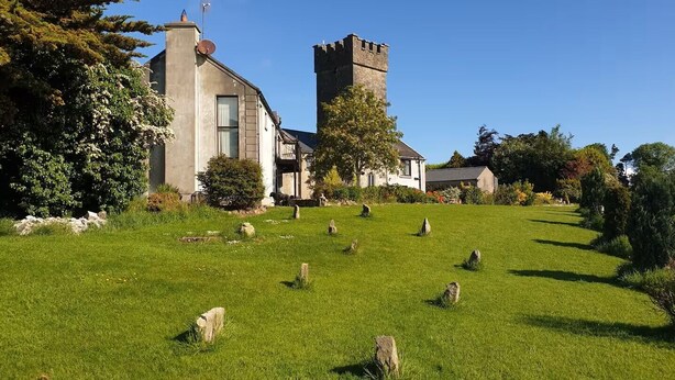 Un edificio con una torre, rodeado de un césped con piedras delimitadoras.