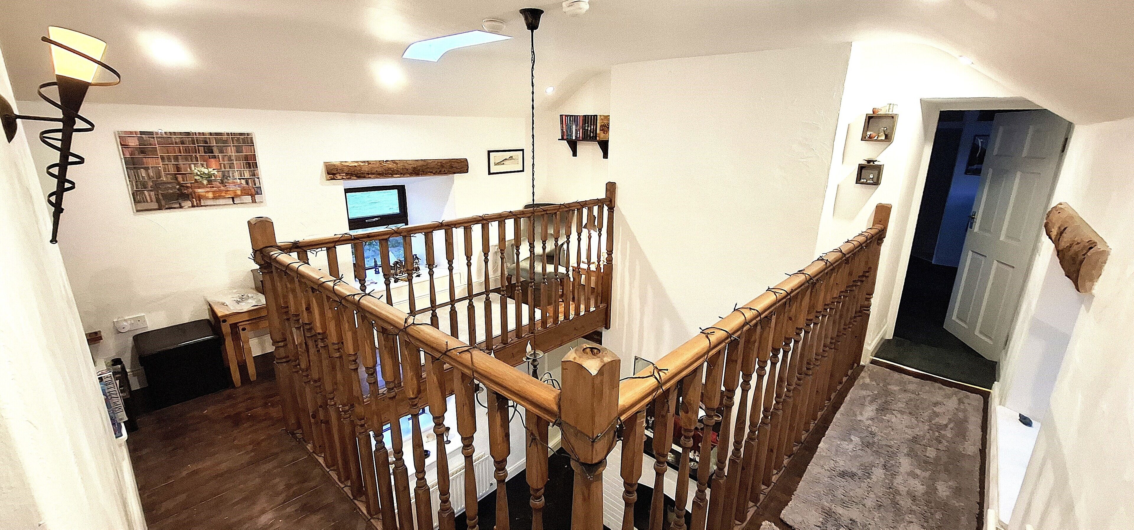 A staircase with wooden balusters and a handrail, leading to a room with a television, bookshelf, and a window.