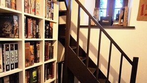 Una escalera con barandilla de madera que lleva a un rellano. Abajo, hay una estantería llena de juegos de mesa.