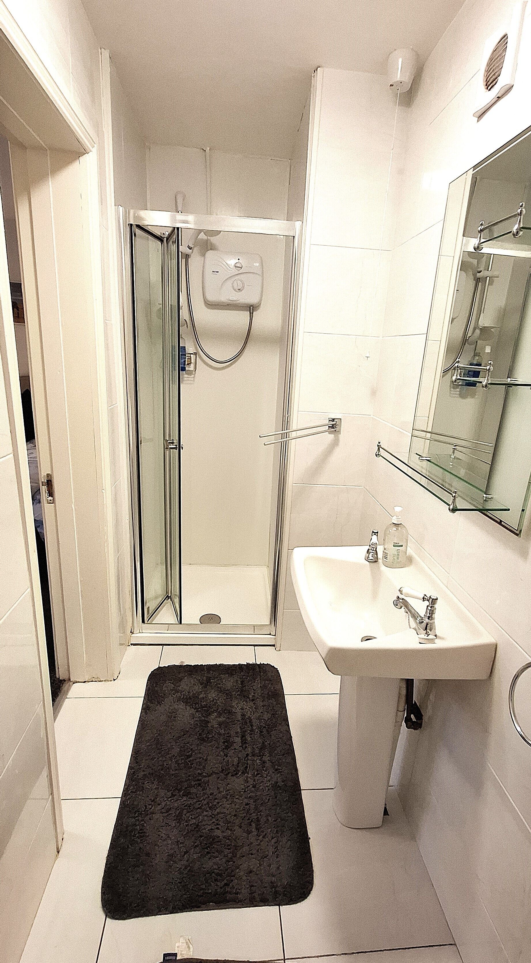 Een badkamer met een douchecabine van glas, een wastafel met spiegel en een zwart vloerkleed.