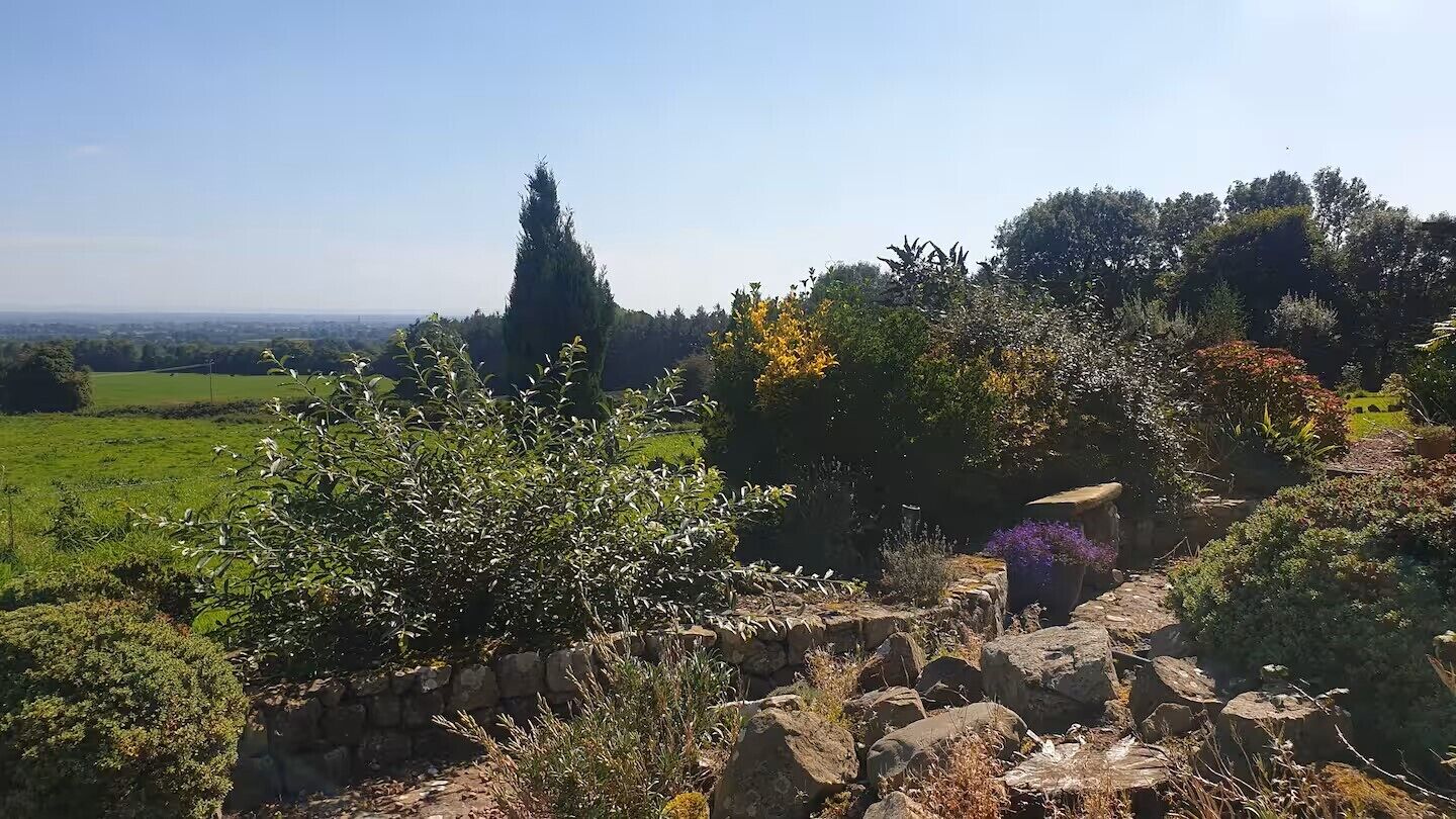 Eine Steinsäule mit einem Gartenpfad, umgeben von verschiedenen Sträuchern und Bäumen.