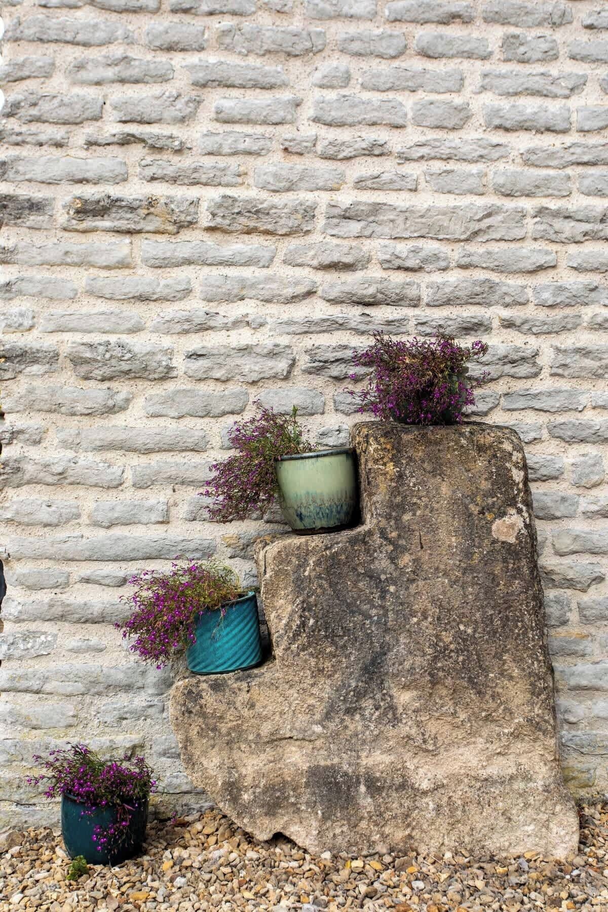 Un muro de piedra con tres macetas que contienen flores moradas.