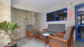 A room with patterned wallpaper, a wooden sofa set, a glass coffee table, and a potted plant. - Travel & Stay (Ootacamund)