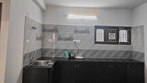 A compact kitchen with a stainless steel sink, black cabinets, and a window with bars. - Travel & Stay (Ootacamund)
