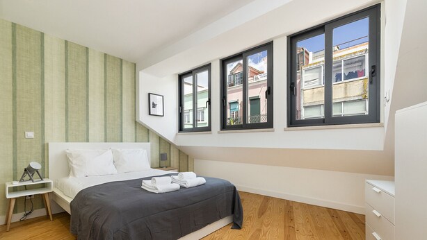 A bedroom with a bed, a nightstand, a dresser, and large windows. - Belem Design 15 by Homing (Lisbon)