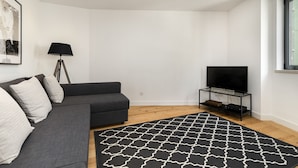 A modern living room with a dark grey sofa, a black floor lamp, a black and white patterned rug, and a flat-screen TV on a black stand. - Belem Design 15 by Homing (Lisbon)