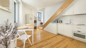 A modern kitchen with white cabinetry, a wooden staircase, and a dining area with a white table and chairs. - Belem Design 15 by Homing (Lisbon)