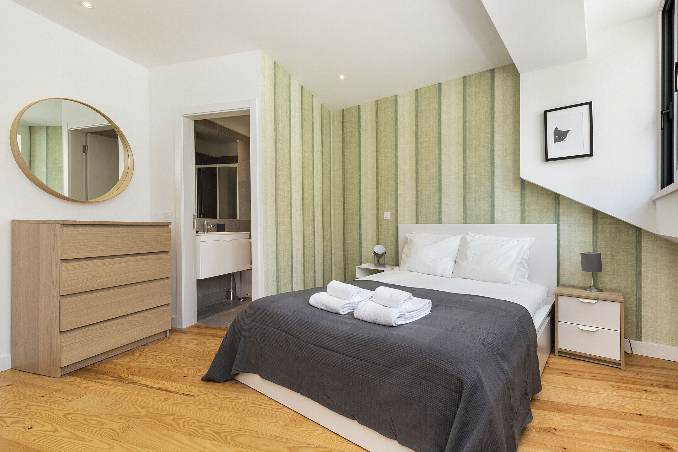 A bedroom with a bed, a dresser, a nightstand, a mirror, and a framed picture on the wall.