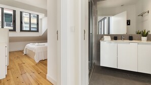 A modern hotel room with a wooden floor, a bed with white linens, a large mirror above the sink, and a small balcony with a view. - Belem Design 14 by Homing (Lisbon)