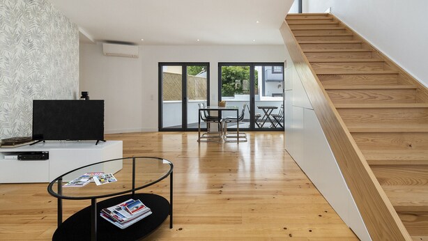 A modern living room with a wooden staircase, a flat-screen TV on a white cabinet, and a dining area with a table and chairs. - Belem Design 14 by Homing (Lisbon)