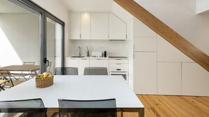 A modern kitchen with white cabinets, a wooden staircase, and a dining area with a white table and chairs. - Belem Design 14 by Homing (Lisbon)