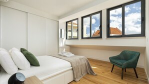 Un dormitorio con cama, una silla y ventanas amplias.