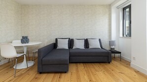 Una sala de estar moderna con un sofá seccional gris, una mesa redonda blanca y una mesita de noche con una lámpara.