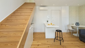 Una cocina moderna con escalera de madera, una pequeña isla con pileta y un comedor con mesa y sillas.