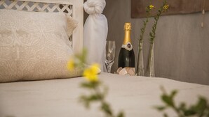 A bed with a decorative pillow, a bottle of champagne, and two vases with flowers. - Grootvlei Guest Farm (Cederberg)