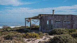 A stone building with a pergola, a view of the ocean, and a sandy landscape.