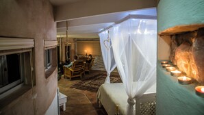 A bedroom with a canopy bed, a small table with chairs, and a lit fireplace.
