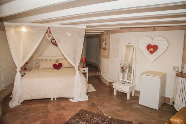 A bedroom with a canopy bed, a small bedside table, a mirror, and a heater.
