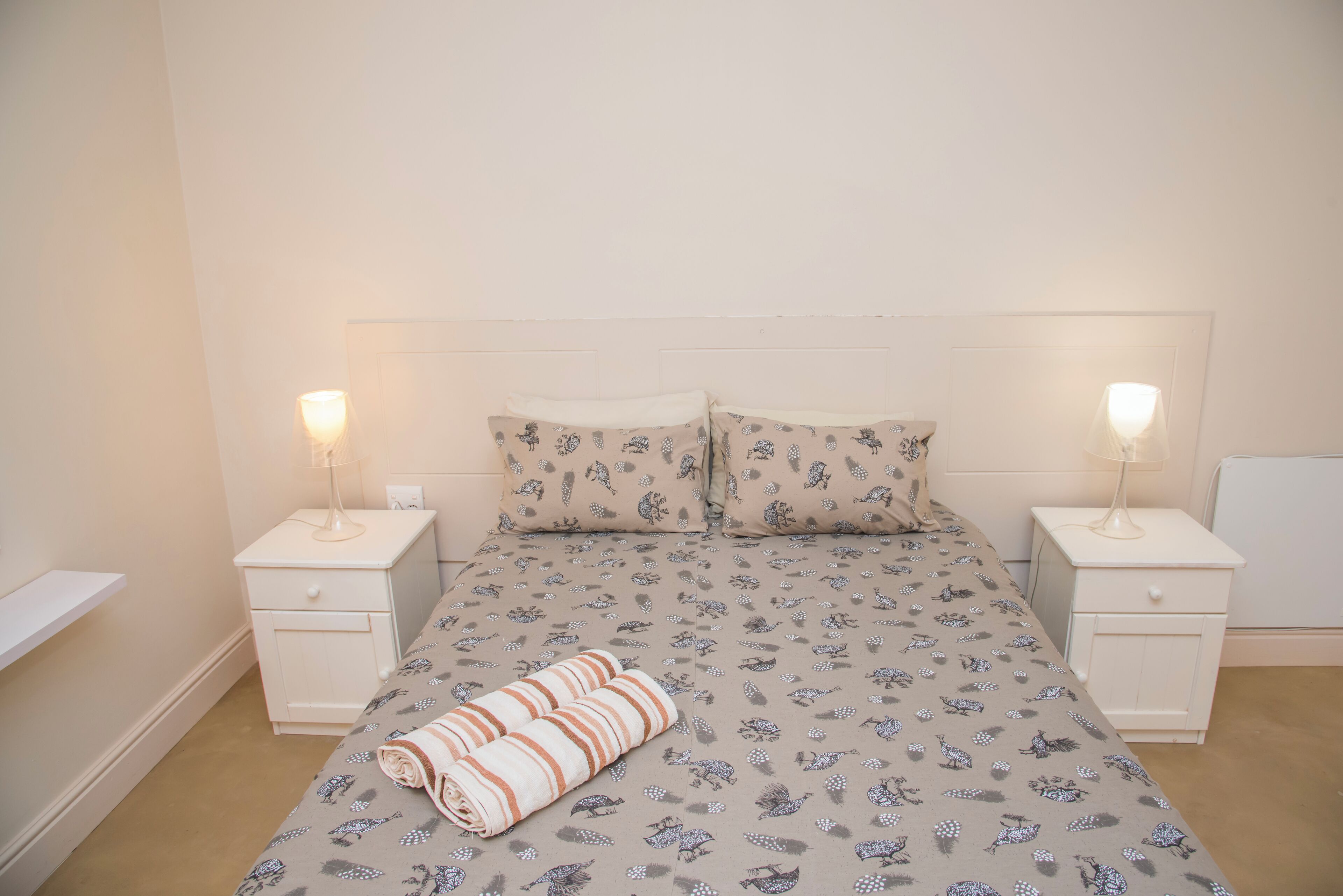 Una cama bien hecha con ropa de cama estampada, dos mesitas de noche con lámparas y un cabecero blanco.