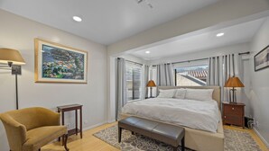 Un dormitorio con cama, una silla, un banco, una mesita de noche y una lámpara.