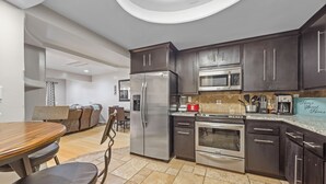 Una cocina moderna con armarios oscuros, electrodomésticos de acero inoxidable y un comedor con mesa y sillas de madera.