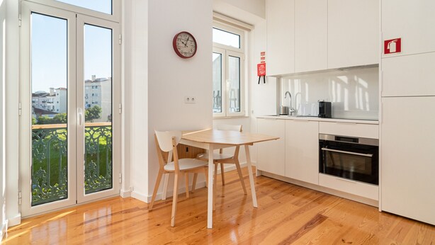 Una cocina moderna con armarios blancos, una mesa de comedor de madera y sillas. Hay un reloj en la pared y un letrero de extintor.