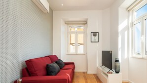 Una sala de estar moderna con un sofá rojo, un televisor de pantalla plana, una mesita y una ventana con persianas.