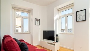 Una sala de estar moderna con un sofá rojo, un televisor de pantalla plana sobre un soporte blanco y ventanas grandes con marcos blancos.