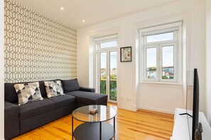 Una sala de estar moderna con un sofá modular, una mesa de centro de vidrio y un ventanal con vista a edificios.