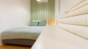 A neatly made bed with a light-colored duvet and pillows, a bedside table with a folded white towel, and a wall with vertical stripes and an air conditioning unit. - Arroios Concept IV by Homing (Lisbon)