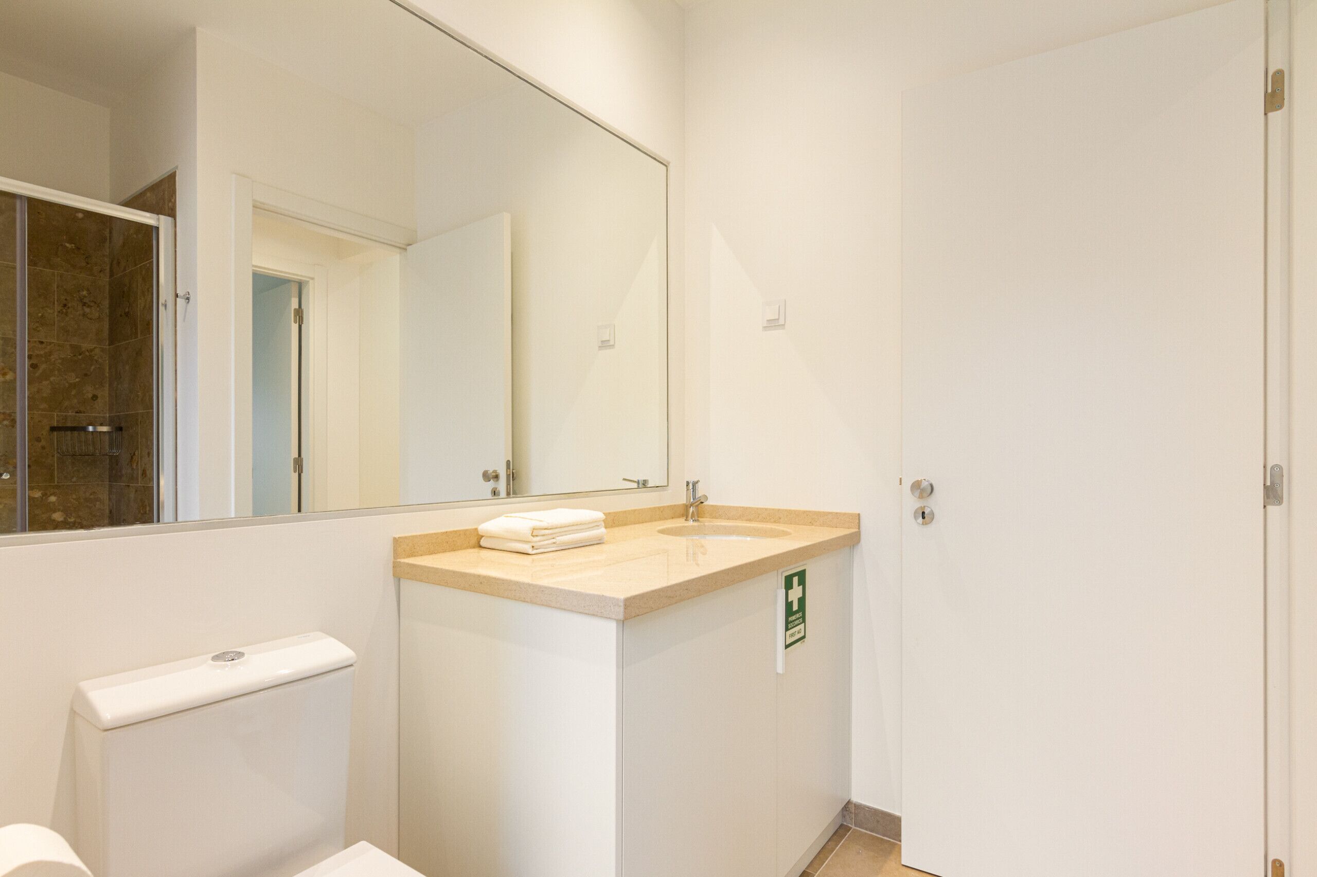 A bathroom with a toilet, sink, and mirror. There is a towel on the sink counter.