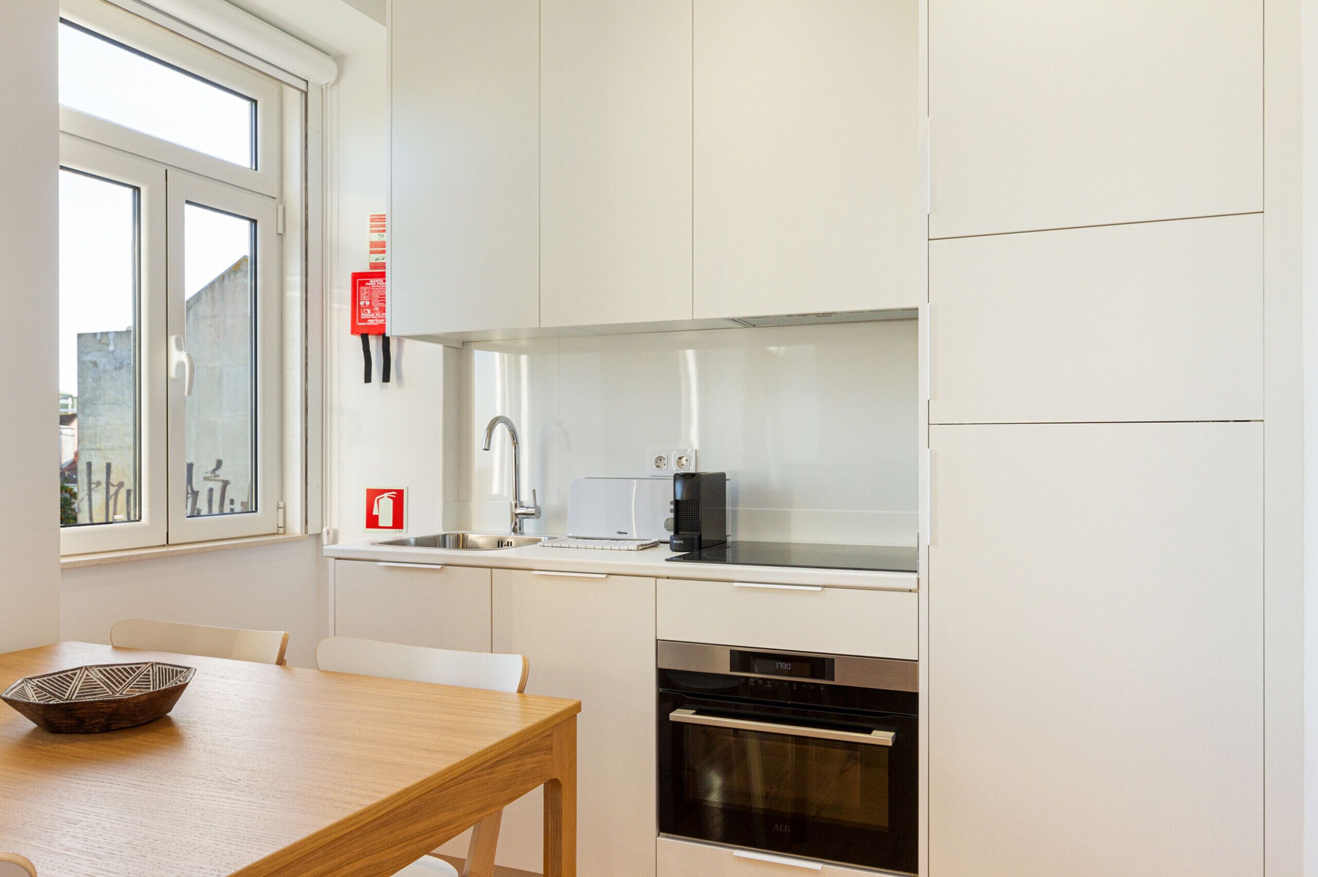 Una cocina moderna con armarios blancos, una campana de acero inoxidable, horno empotrado y ventana con vistas al exterior.